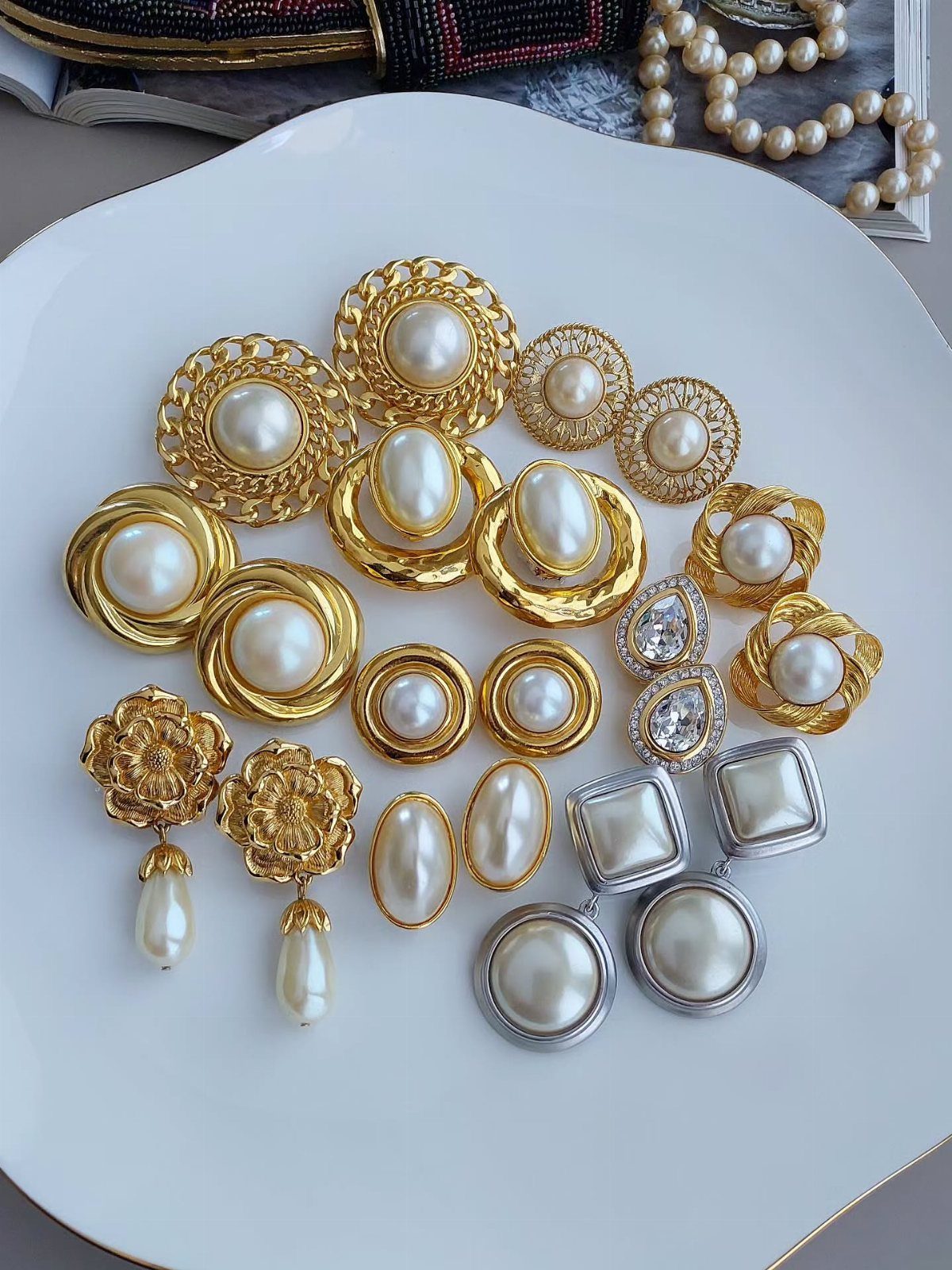 Vintage style pearl and rhinestone earrings arranged on a white ceramic plate.