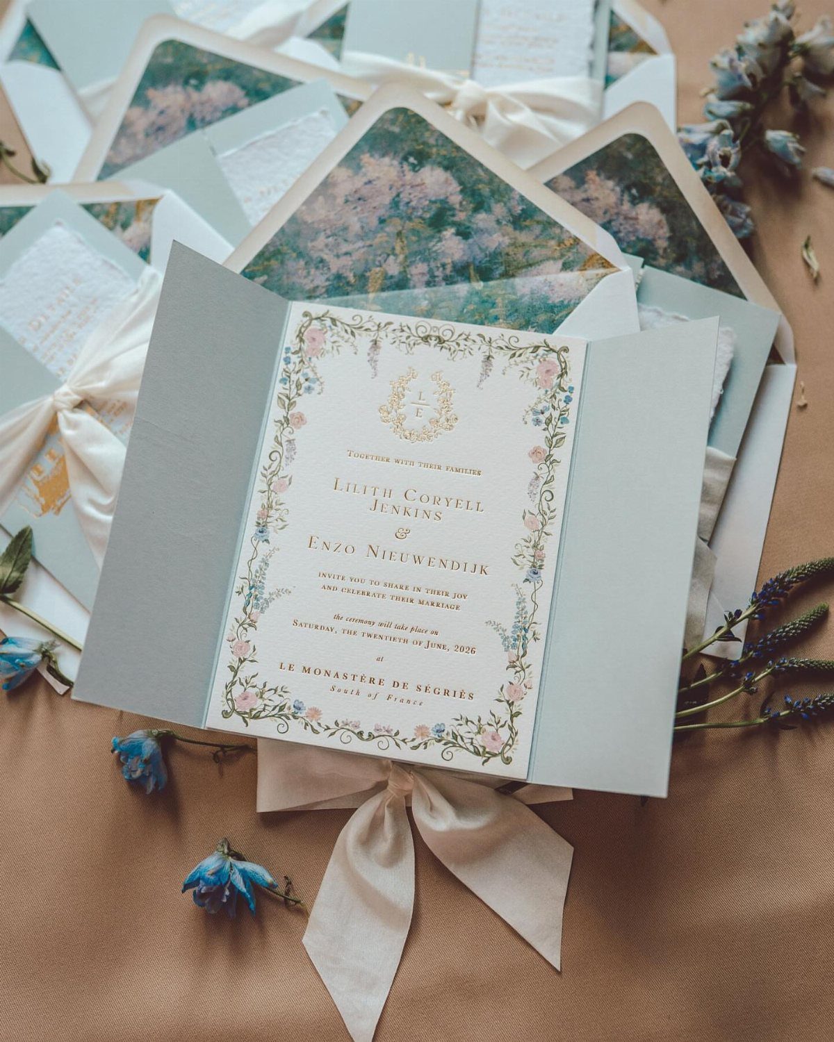 Wedding invitation with botanical floral borders and a light blue envelope tied with ribbon.