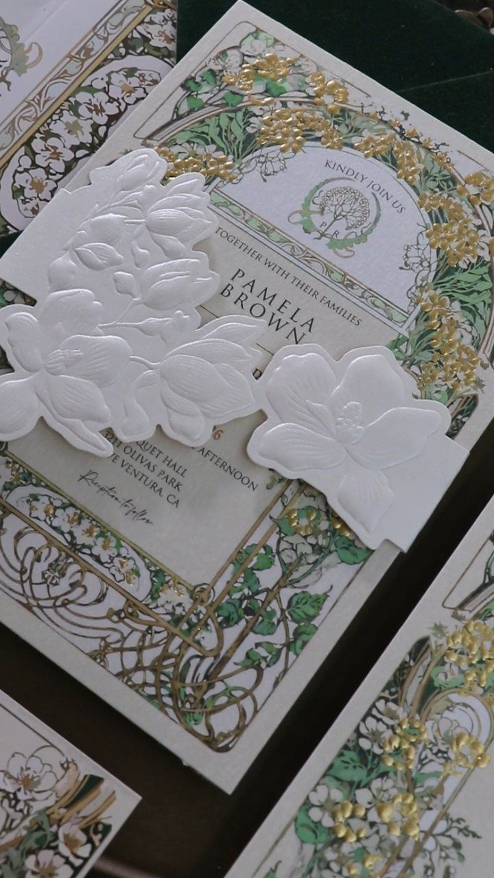 Wedding invitation with ornate green floral borders and white embossed flower cutouts.