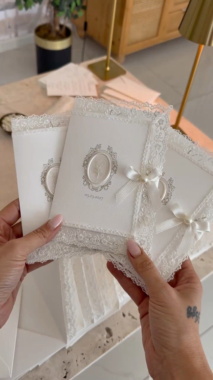 White wedding invitations with lace borders, pearl bows, and embossed oval seals.