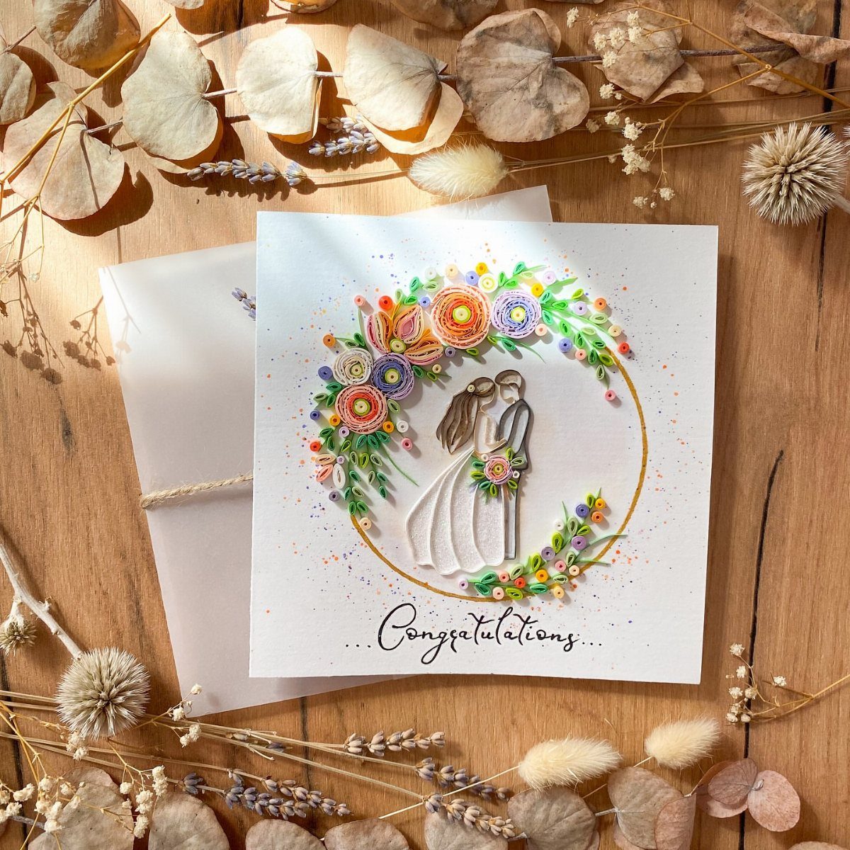 Wedding card with quilled paper art of a couple and colorful floral wreath