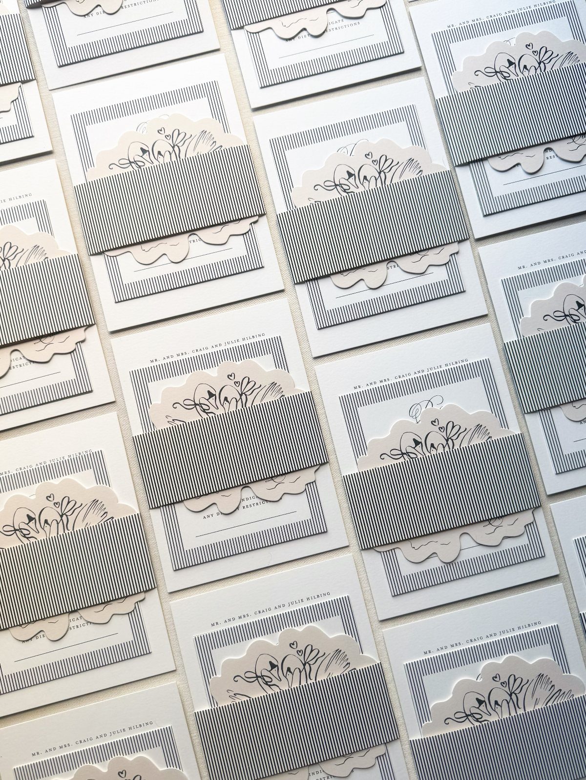 White wedding invitation cards with grey striped bands and floral paper cutouts.