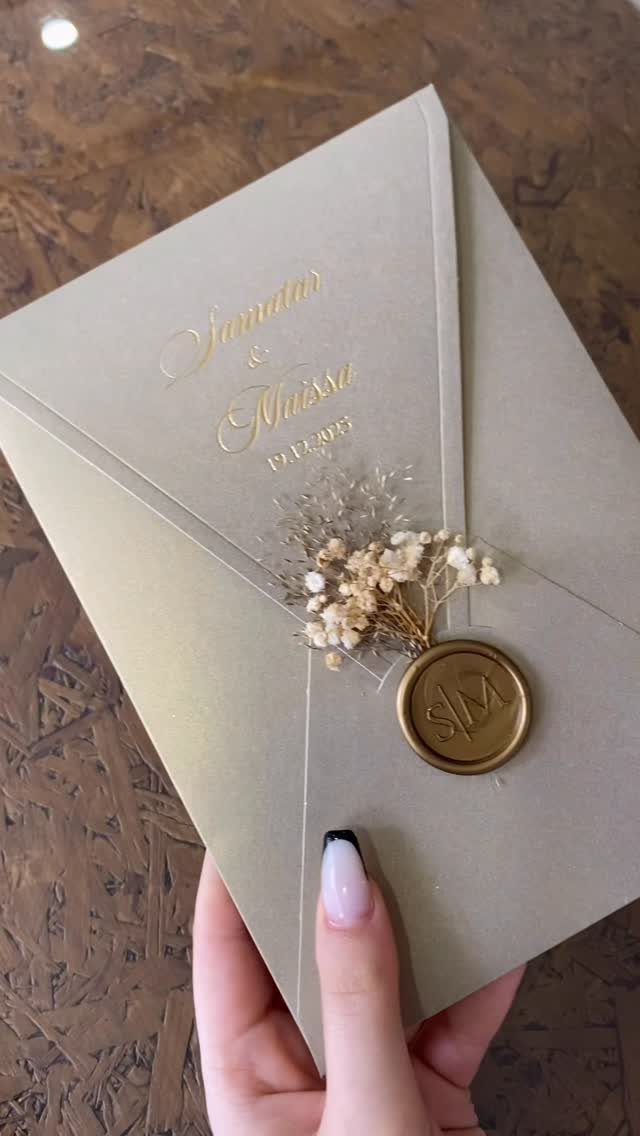 Beige wedding invitation envelope with gold calligraphy, wax seal, and dried flowers.