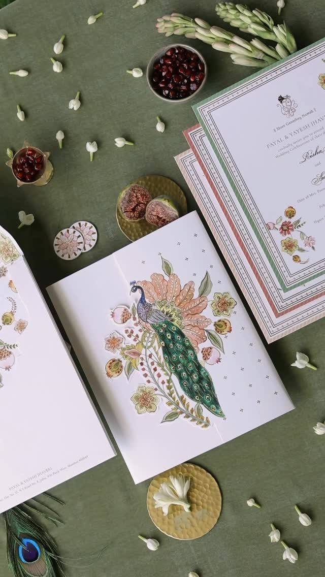 Wedding invitation cards featuring a peacock and floral motifs on green fabric.
