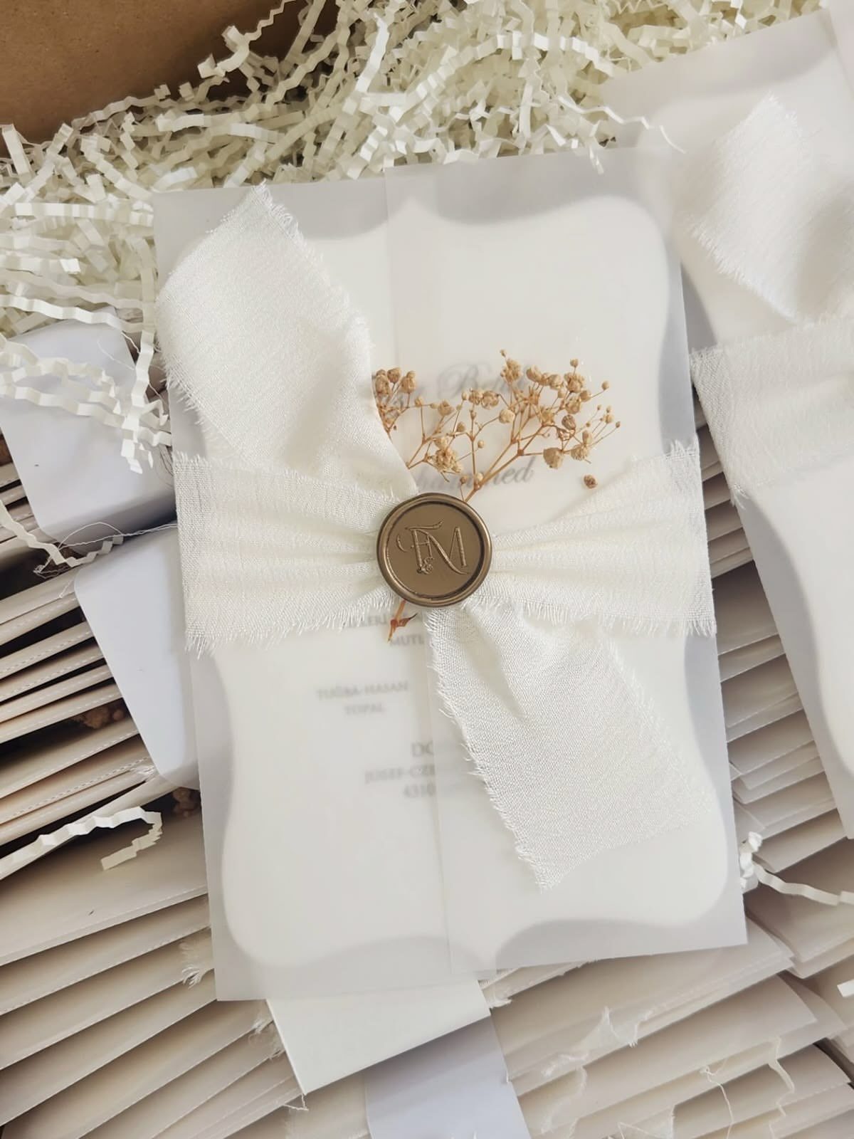 White scalloped wedding invitations wrapped in vellum and ribbon with a gold wax seal.