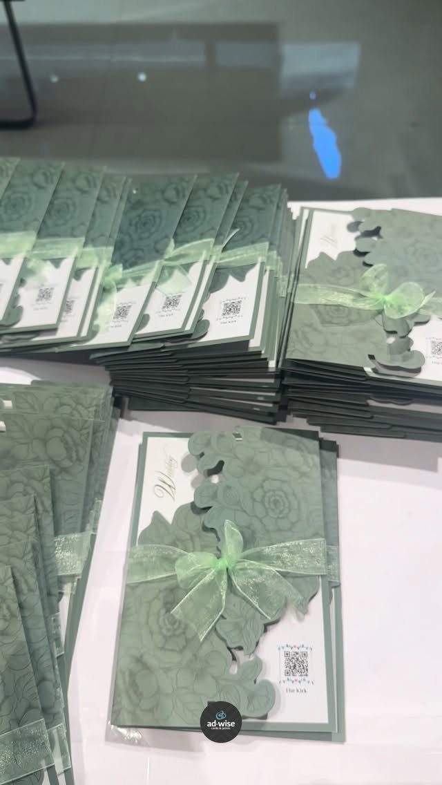 Sage green floral wedding invitations with laser-cut edges and sheer green ribbon bows.
