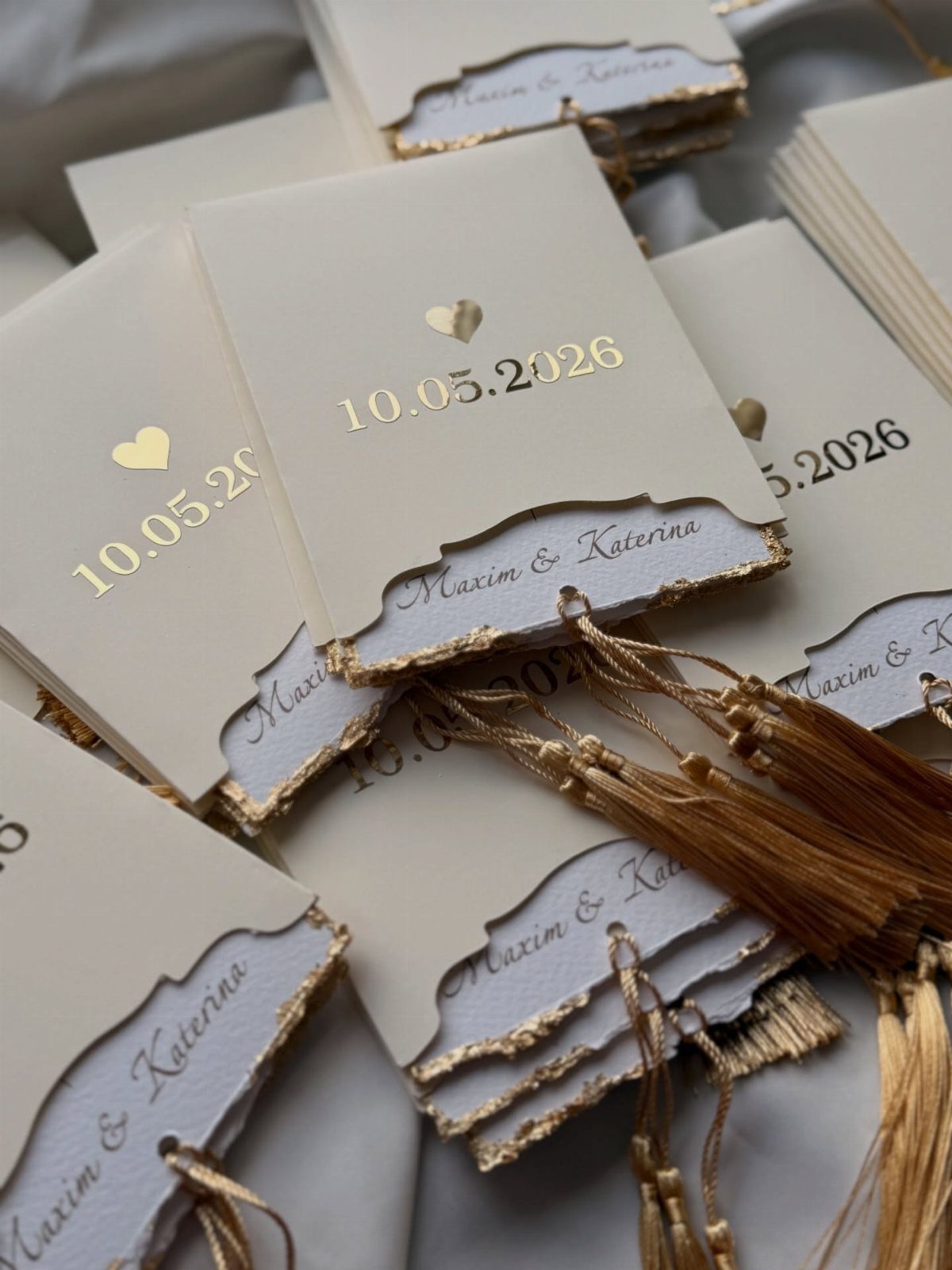 Cream wedding invitations with gold foil text, gilded deckled edges, and gold tassels.