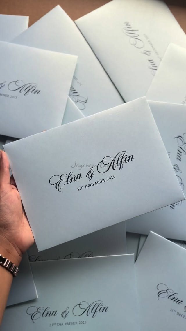 White wedding invitation cards with elegant black cursive calligraphy held by a hand.