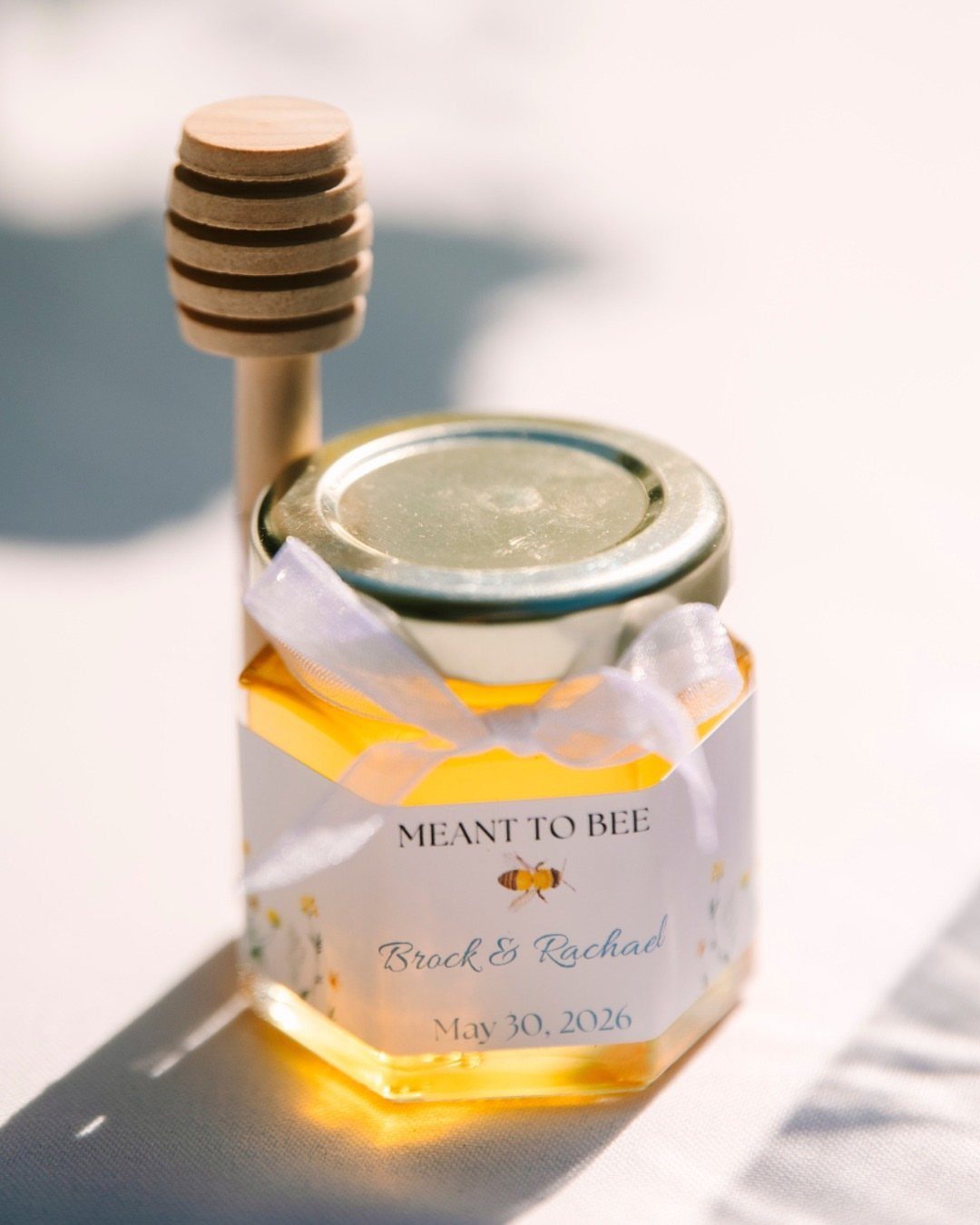 Honey jar wedding favor with a label reading Meant to Bee and honey dipper.