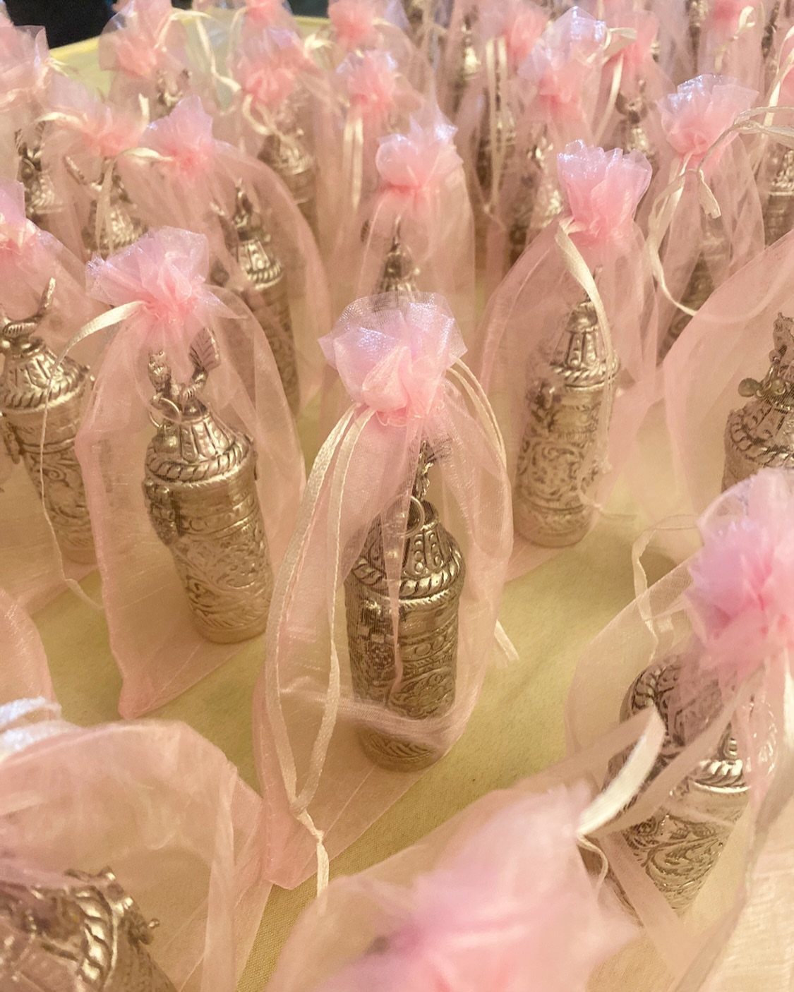 Ornate silver containers in pink organza bags arranged as wedding favors.