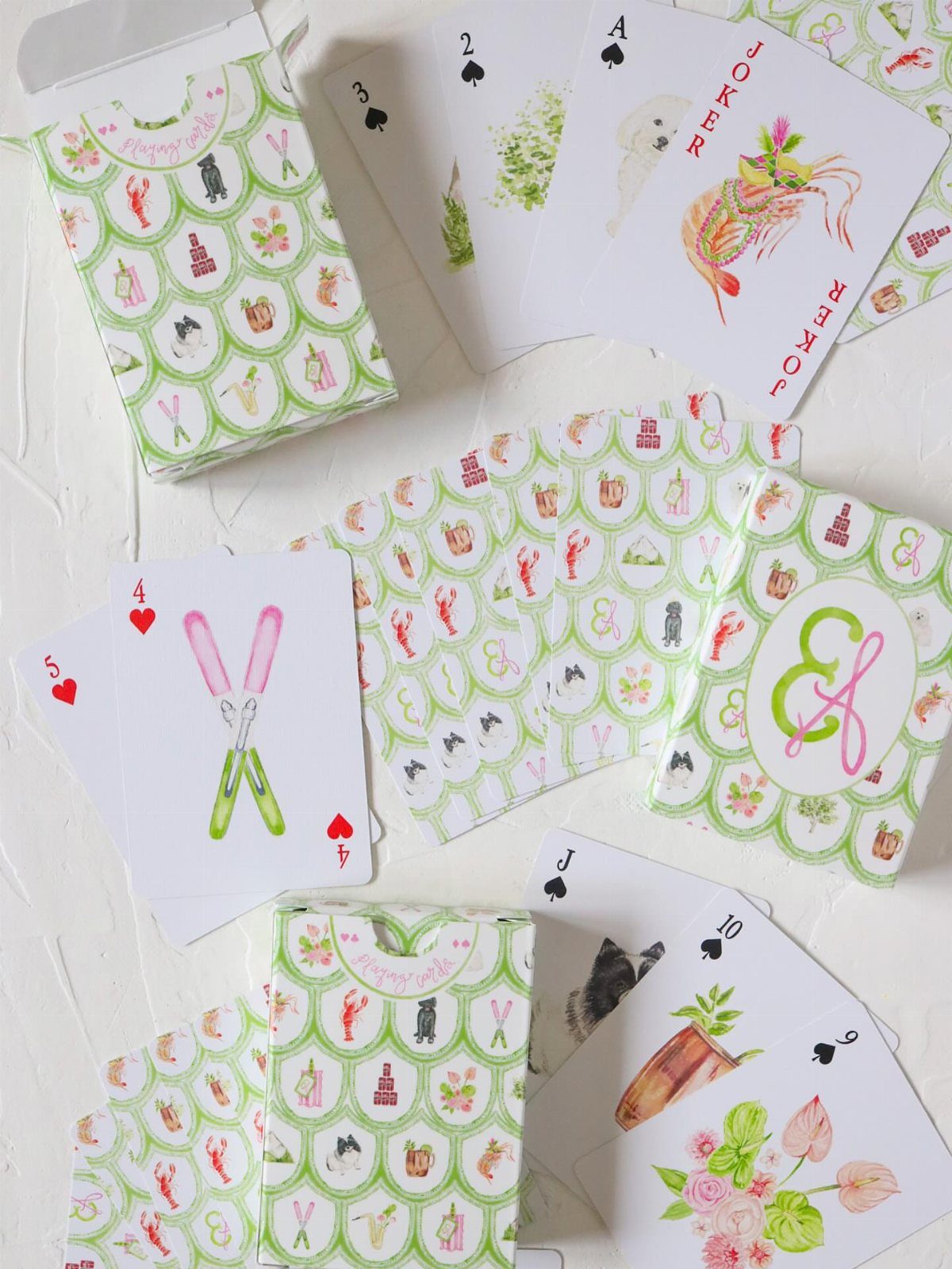 Monogrammed playing cards and patterned green boxes with colorful illustrations on white background