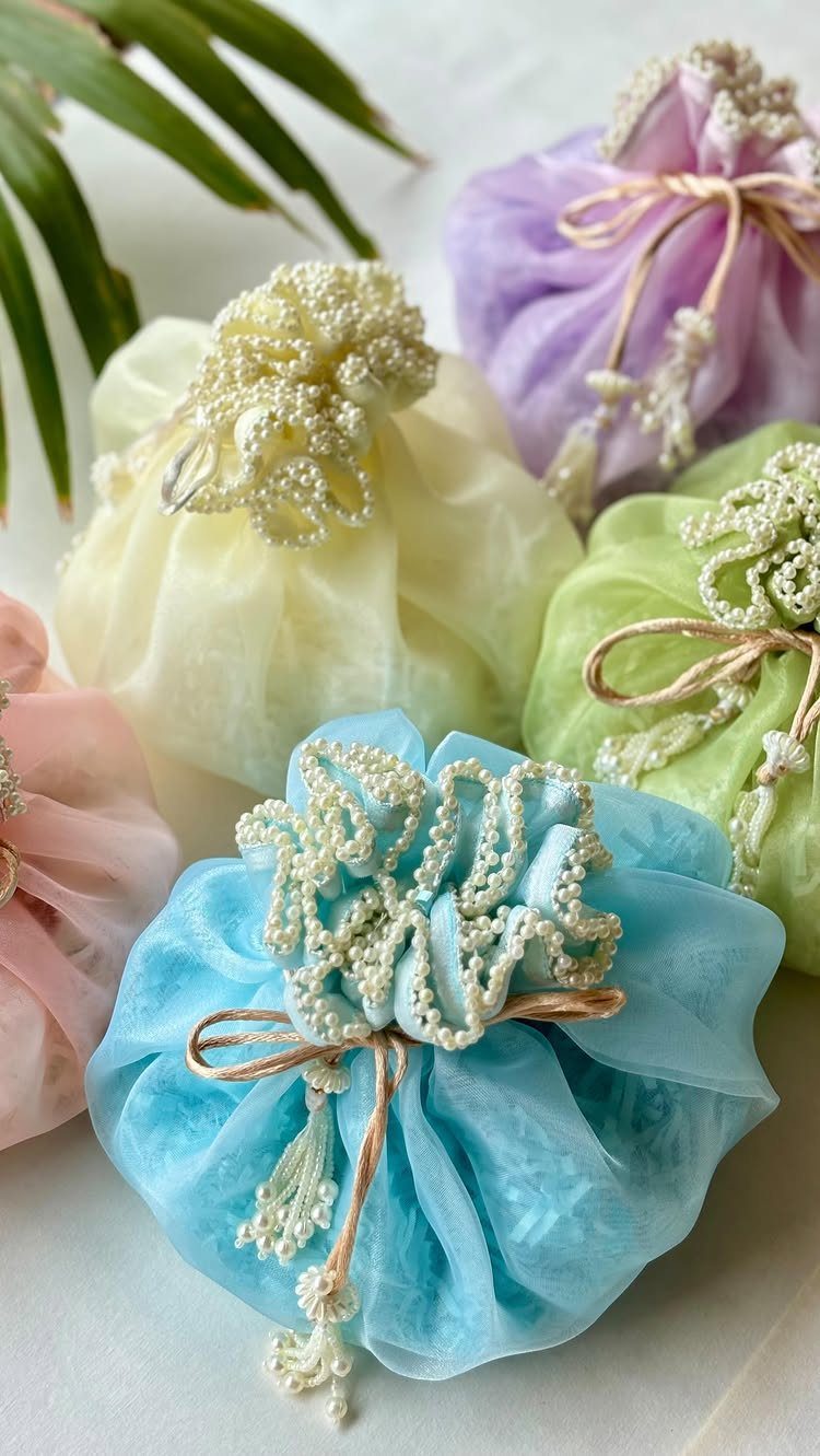 Colorful fabric potli bags with pearl embellishments and gold ties on white surface