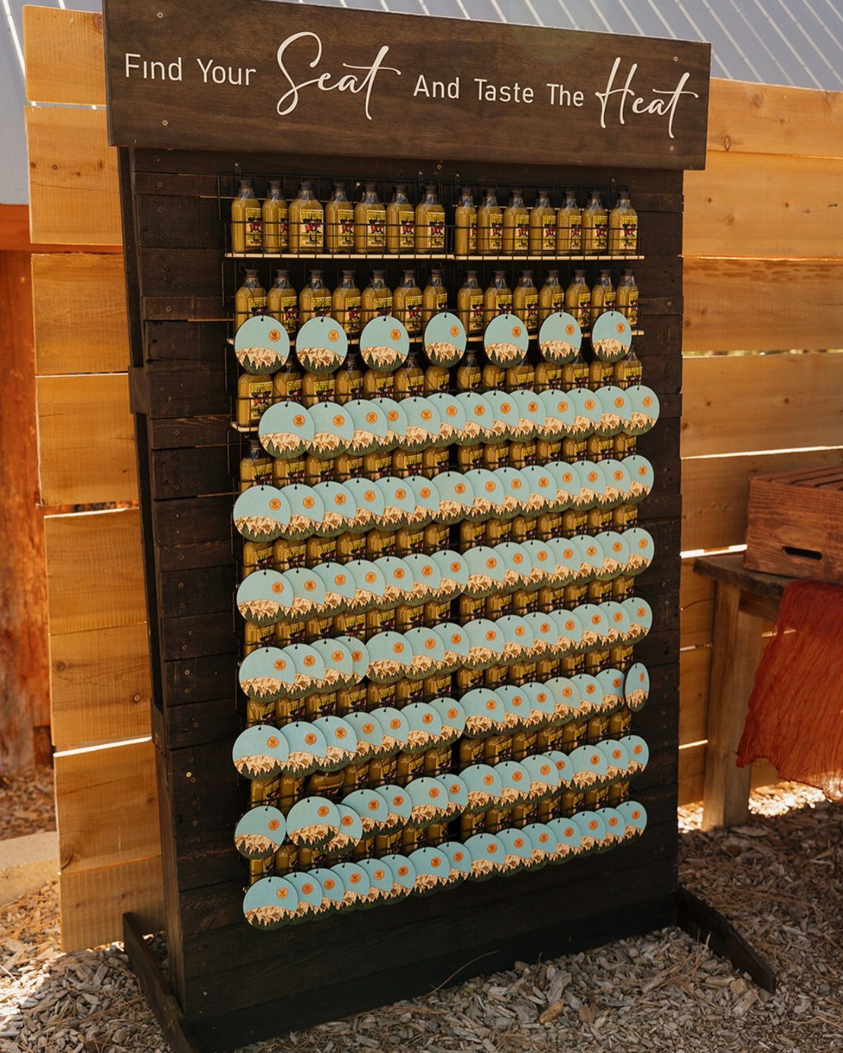 Hot sauce bottles on a wooden display rack with a seating chart banner.