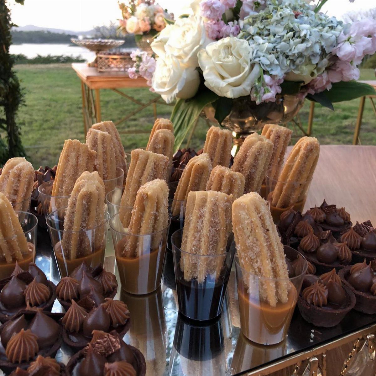 Churros in glasses with chocolate and caramel sauce on a mirrored dessert table