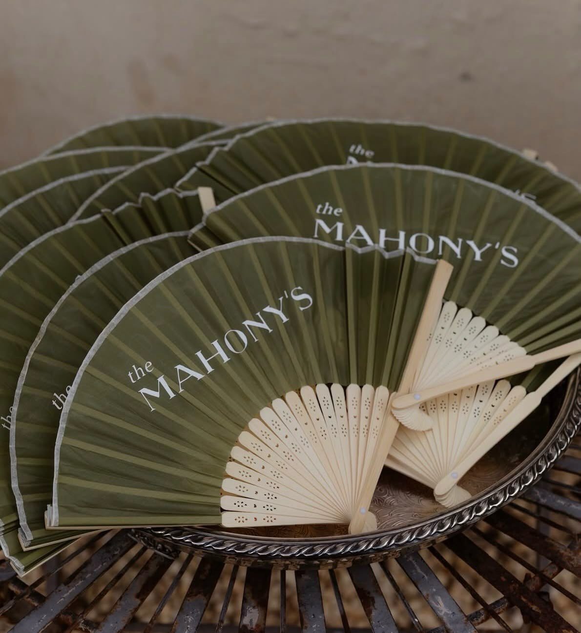 Olive green folding fans with white text resting on a silver tray.