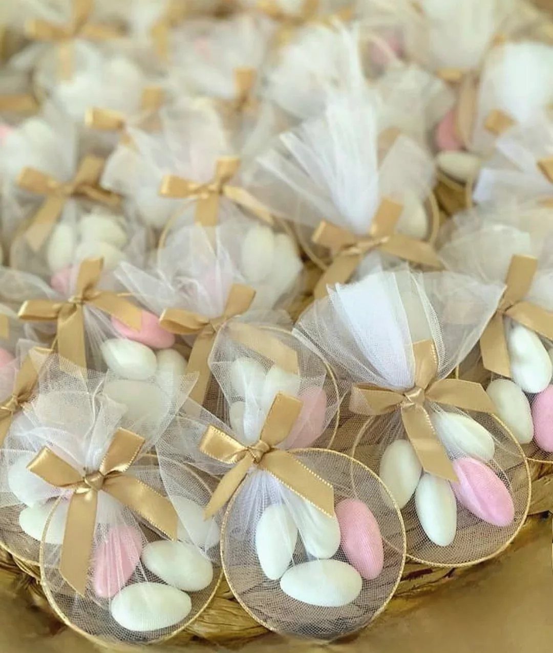 Sugar-coated almonds in white organza bags tied with gold ribbons in a basket