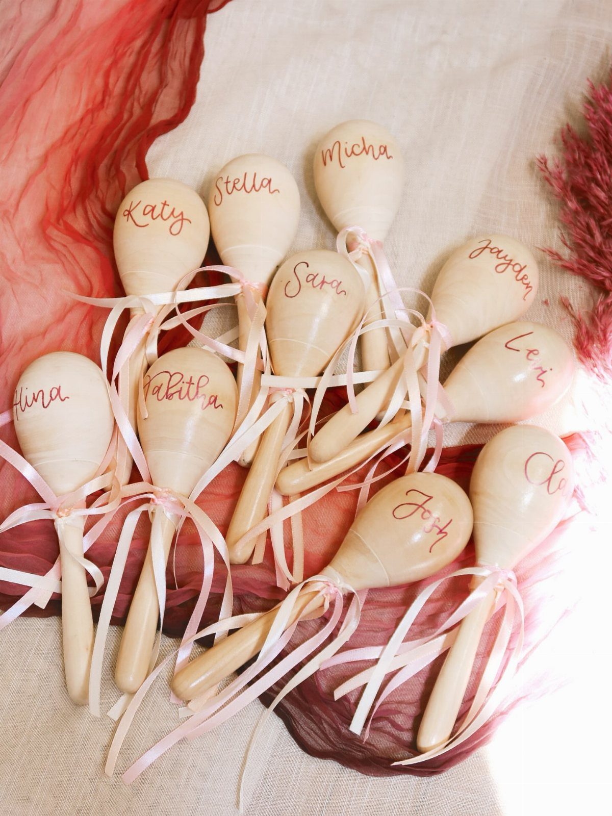 Wooden maracas with personalized names and pink ribbons on red and white fabric