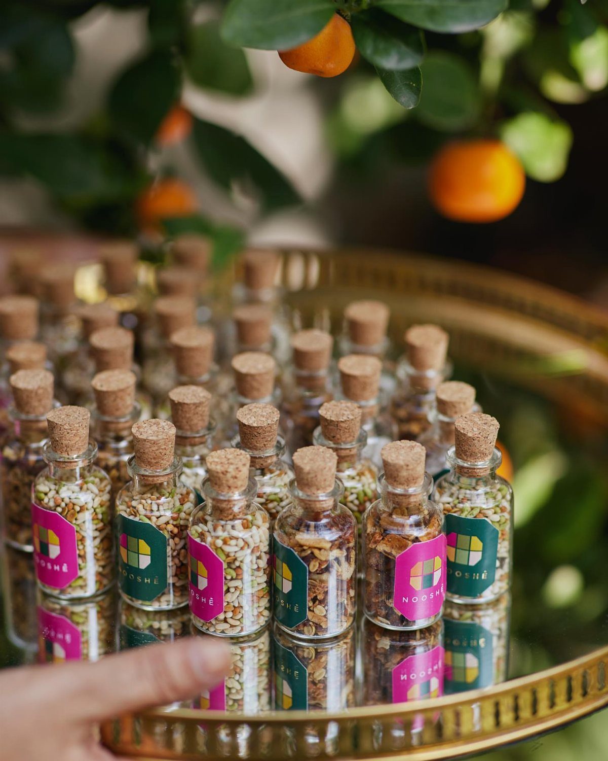 Small glass vials with cork stoppers and colorful labels on a gold tray.