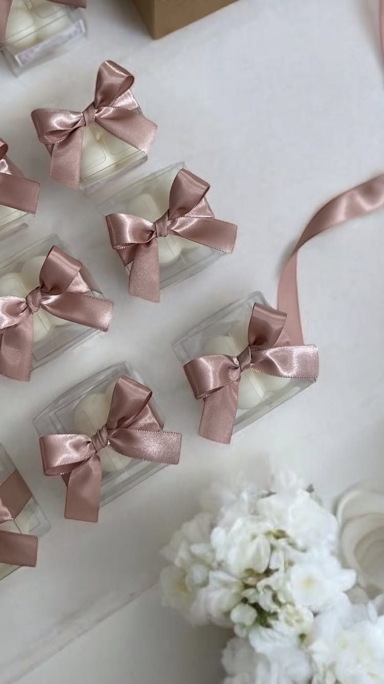 White candles in clear boxes with dusty rose satin bows and white flowers.