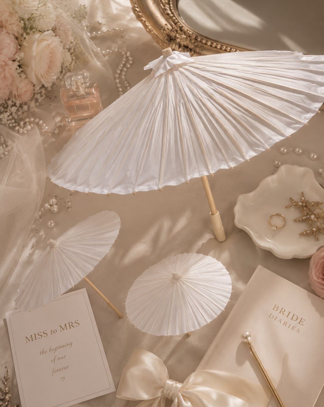 White paper parasols arranged with bridal accessories, pearls, and a bride's diary.