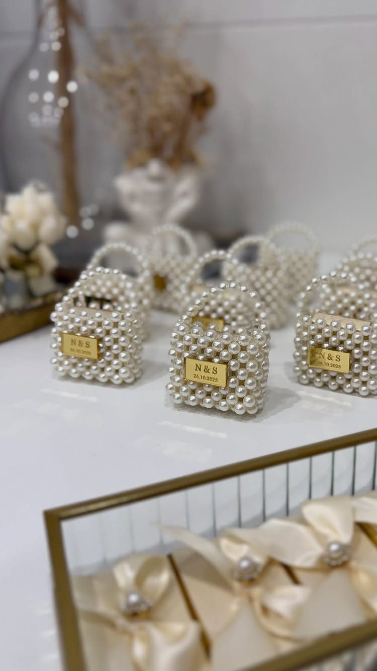 Pearl-beaded white gift bags with gold name tags on a white table