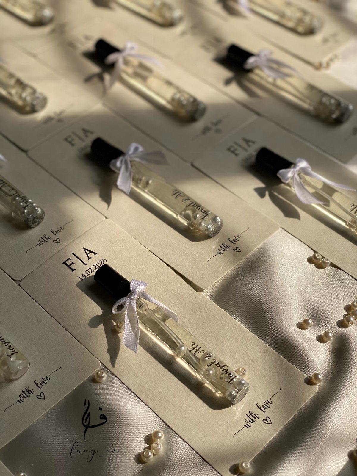 Small perfume bottles with white ribbons on personalized cards over white satin fabric.