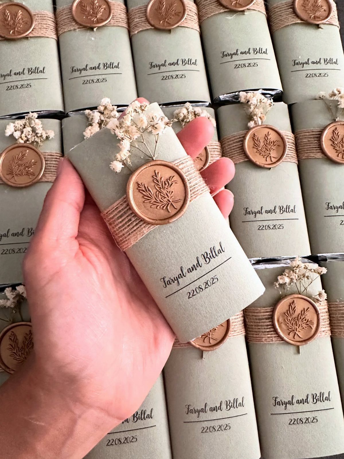 Hand holding a grey wrapped wedding favor with a copper wax seal and flowers