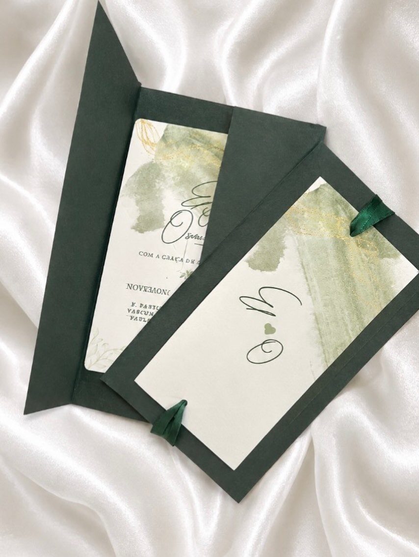 Wedding invitation cards with green watercolor leaves on white satin fabric.