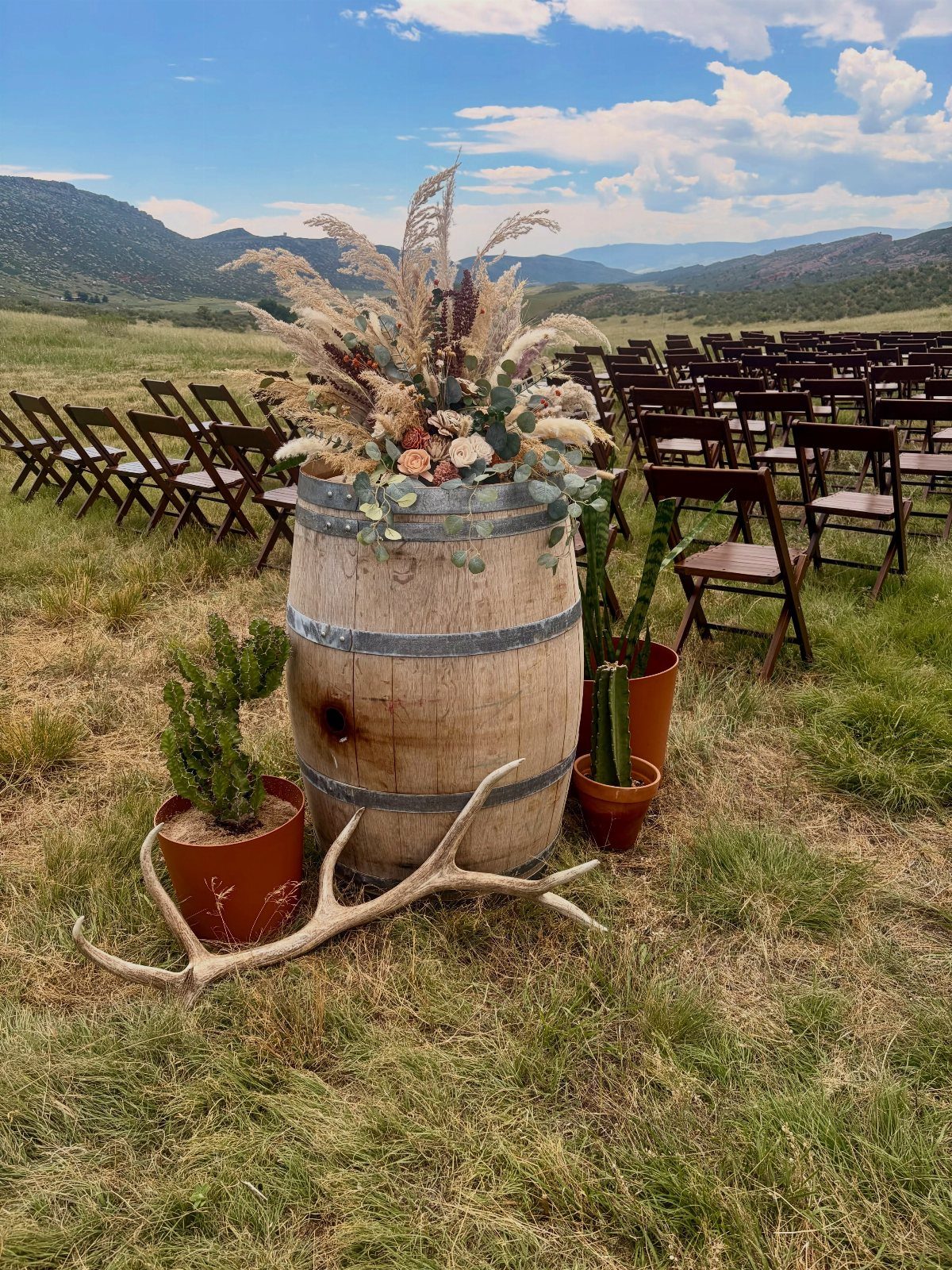 Wooden wine barrel with floral arrangement and antlers in an outdoor wedding setting