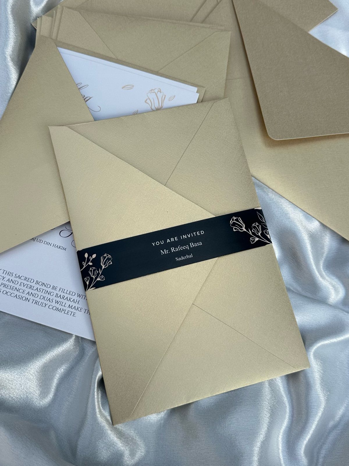 Tan wedding envelopes and white cards on silver satin with a black belly band.