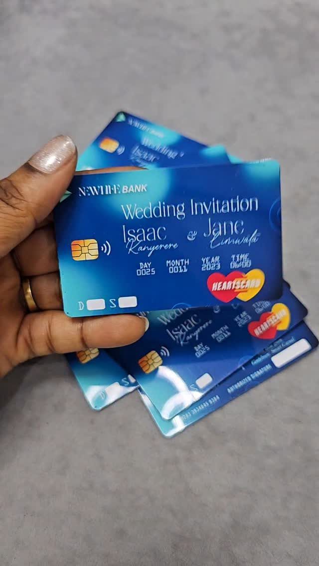 Blue credit card style wedding invitations held by a hand over a grey background