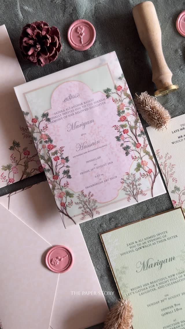 Floral wedding invitations with pink borders and wax seals on a stone surface
