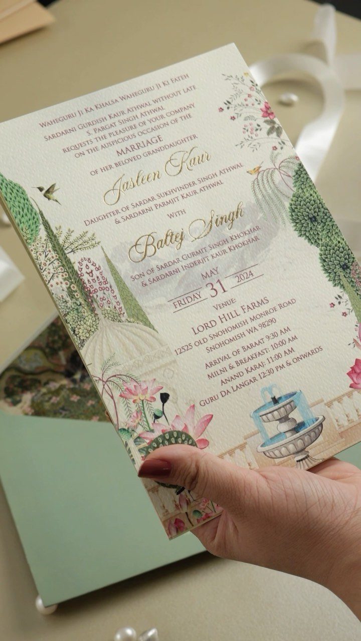 Wedding invitation card with green botanical illustrations held by a hand.
