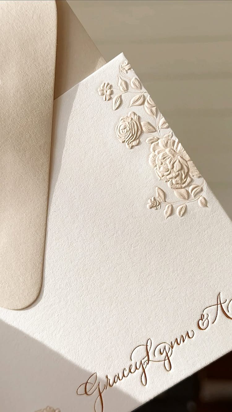 Cream wedding invitation with embossed floral details and gold cursive calligraphy text.