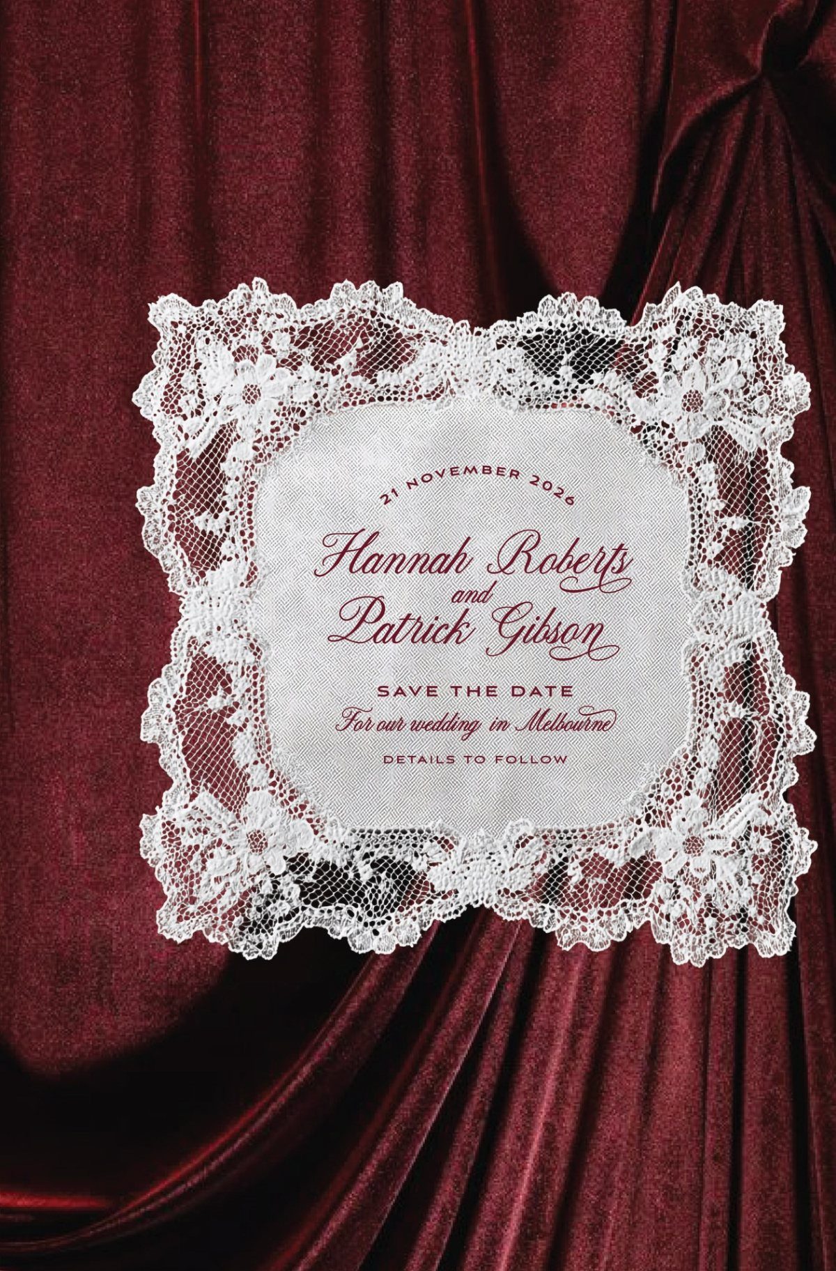 White lace-bordered wedding invitation resting on draped deep red velvet fabric.