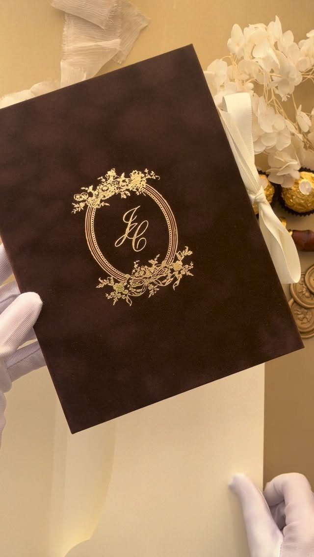 Dark brown invitation card with gold foil-pressed monogram and floral details.
