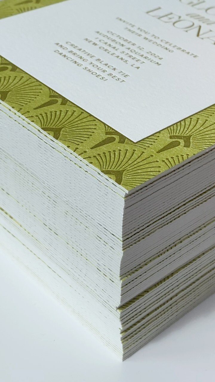 Stack of wedding invitations with green art deco borders and black printed text.