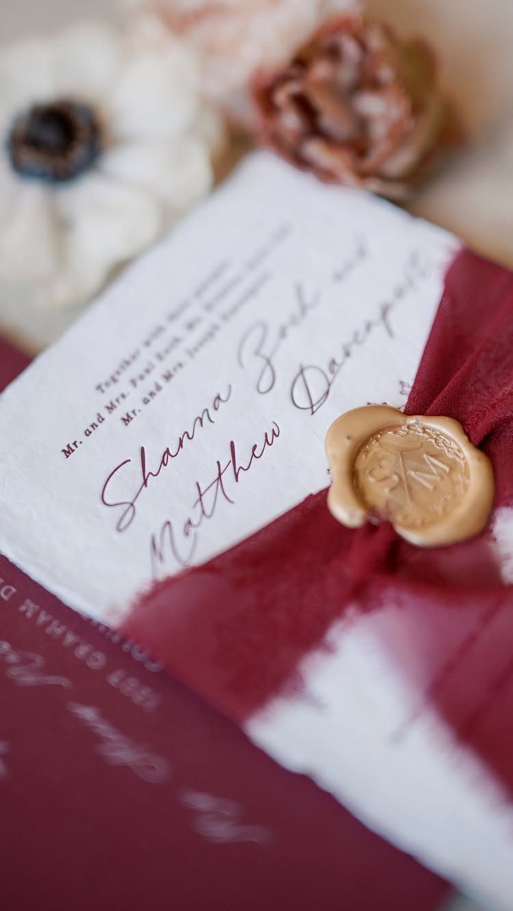 Wedding invitation wrapped in a burgundy fabric belly band with a gold wax seal