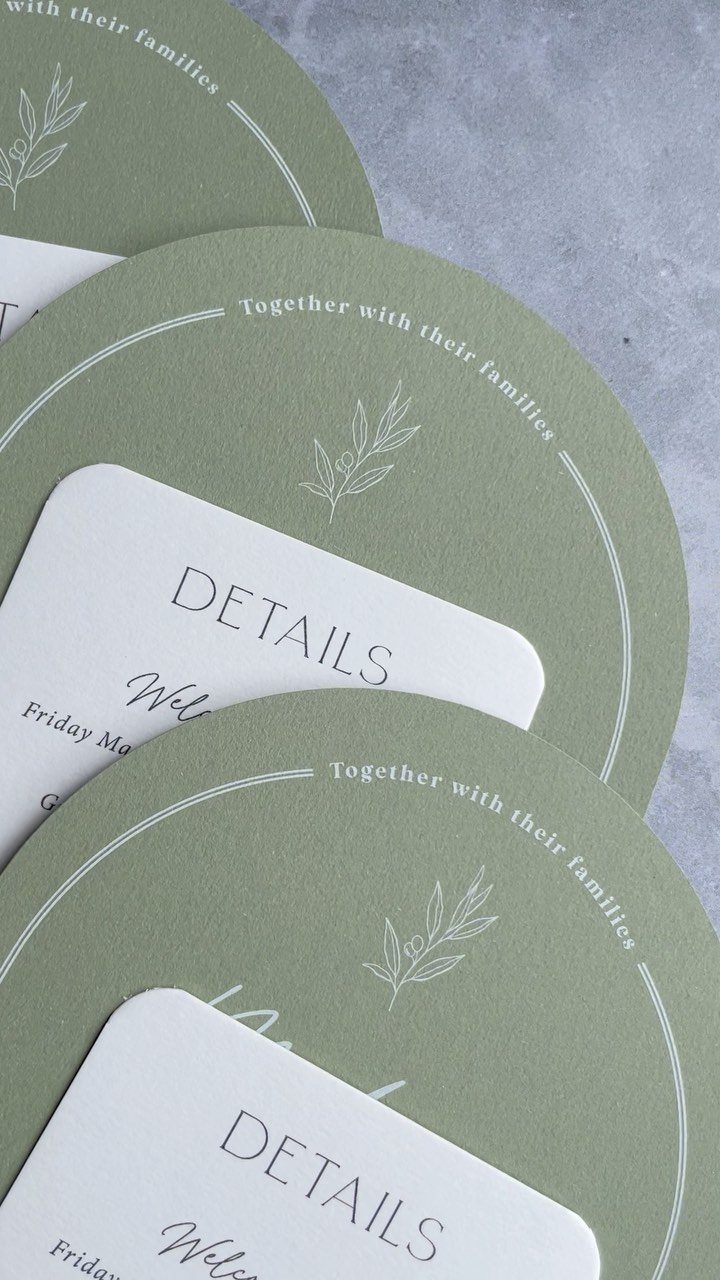 Sage green circular wedding invitations and white detail cards on a grey background.