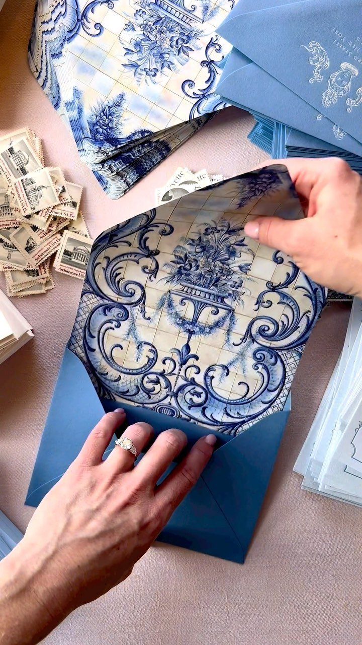 Blue patterned envelope lining being held by hands among wedding stationery and stamps