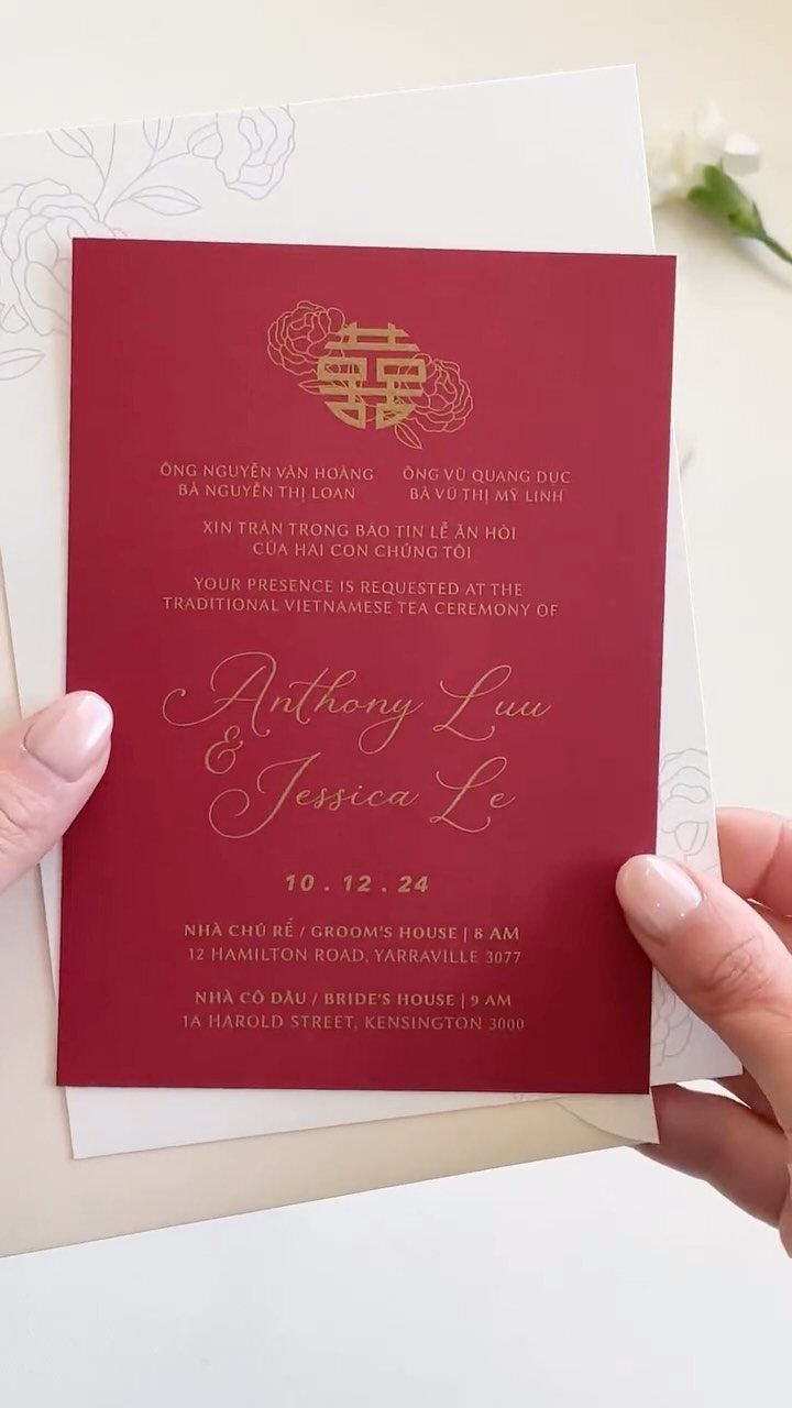 Red wedding invitation with gold foil lettering held over a white floral card.