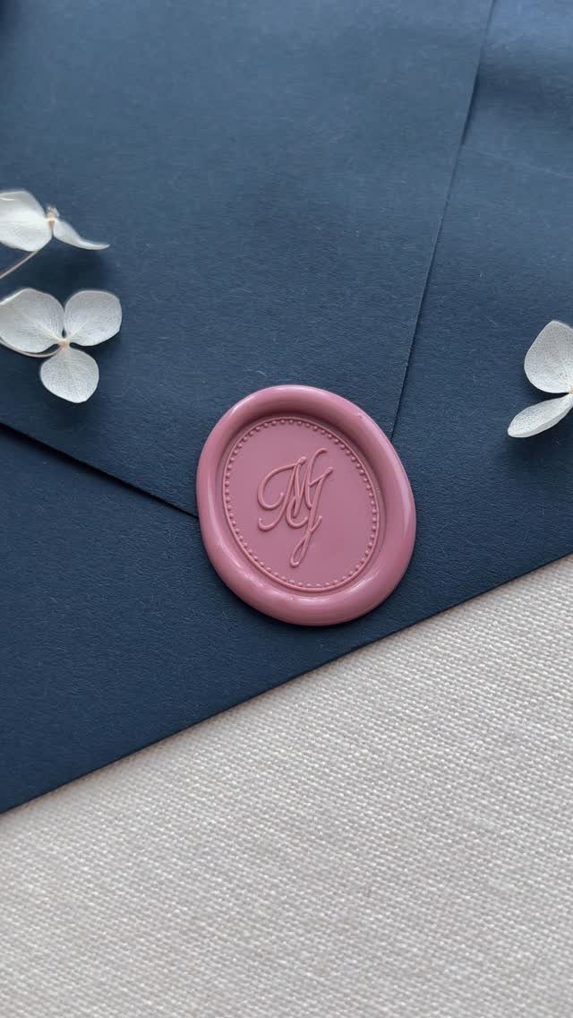 Mauve wax seal with initials on a dark blue envelope with white petals