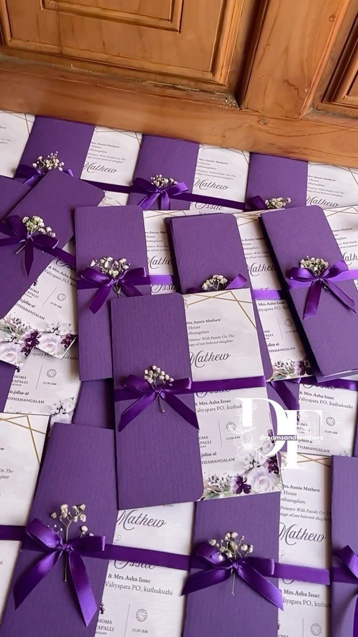 Purple and white wedding invitation sets tied with ribbons and small white flowers.