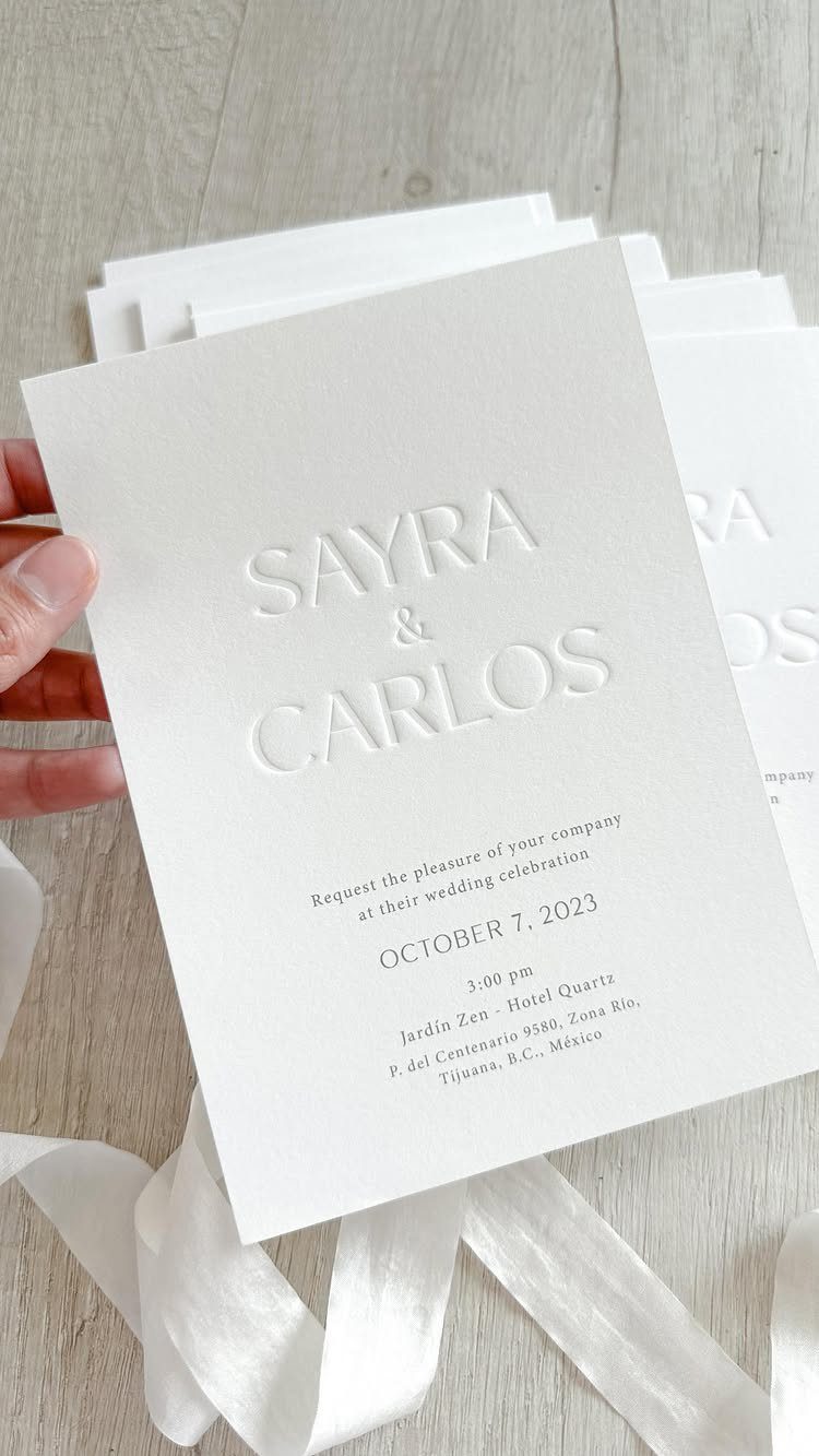 White wedding invitation with blind embossed names and black printed event details.