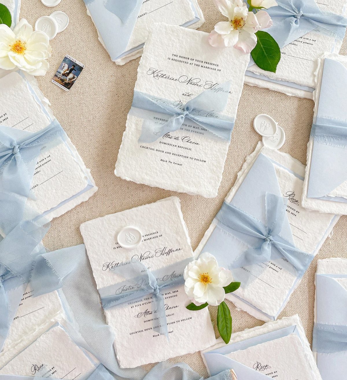 White deckled edge wedding invitations tied with light blue ribbons and white flowers