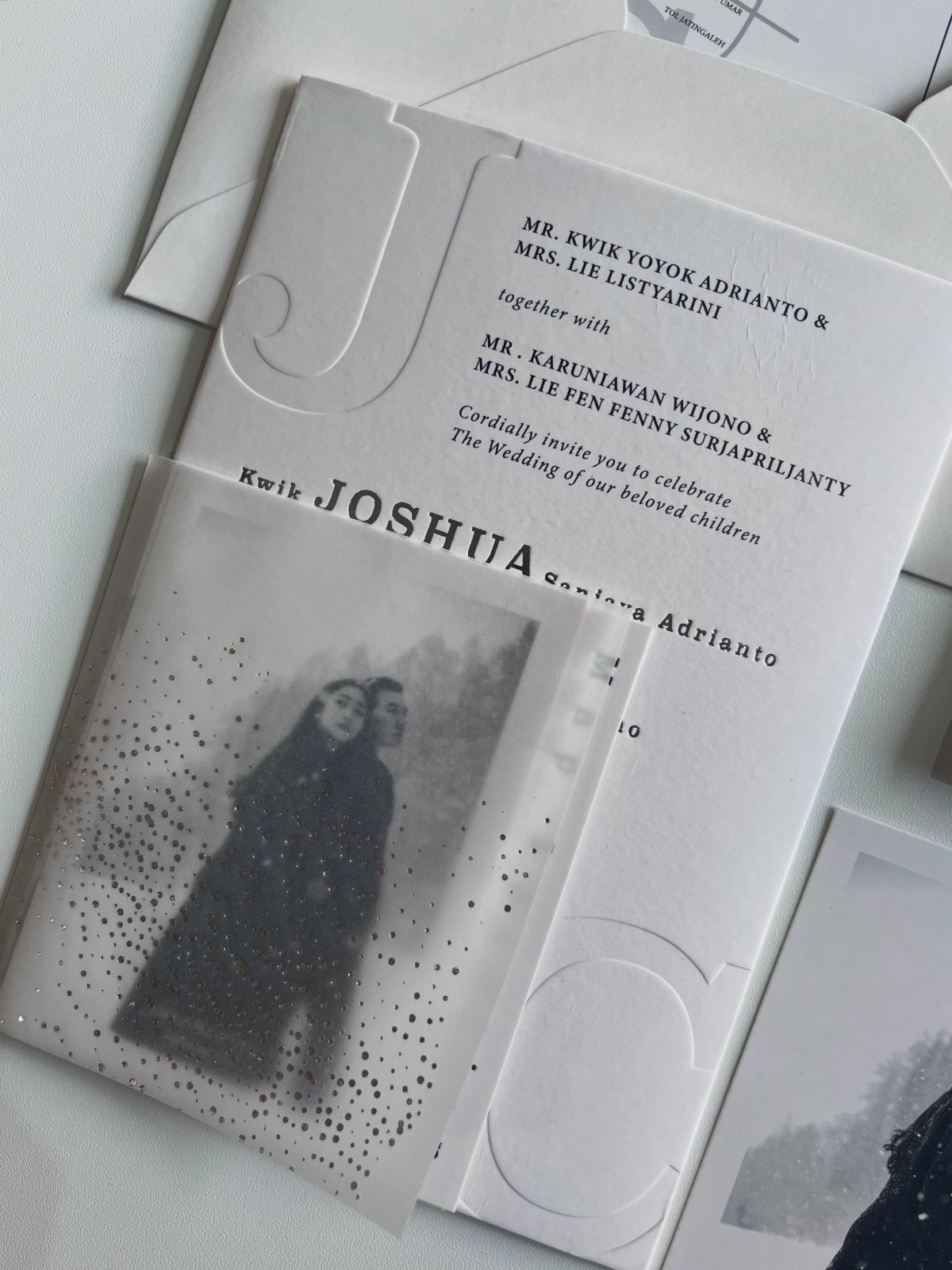 White wedding invitation with embossed lettering and a translucent photo overlay of a couple.