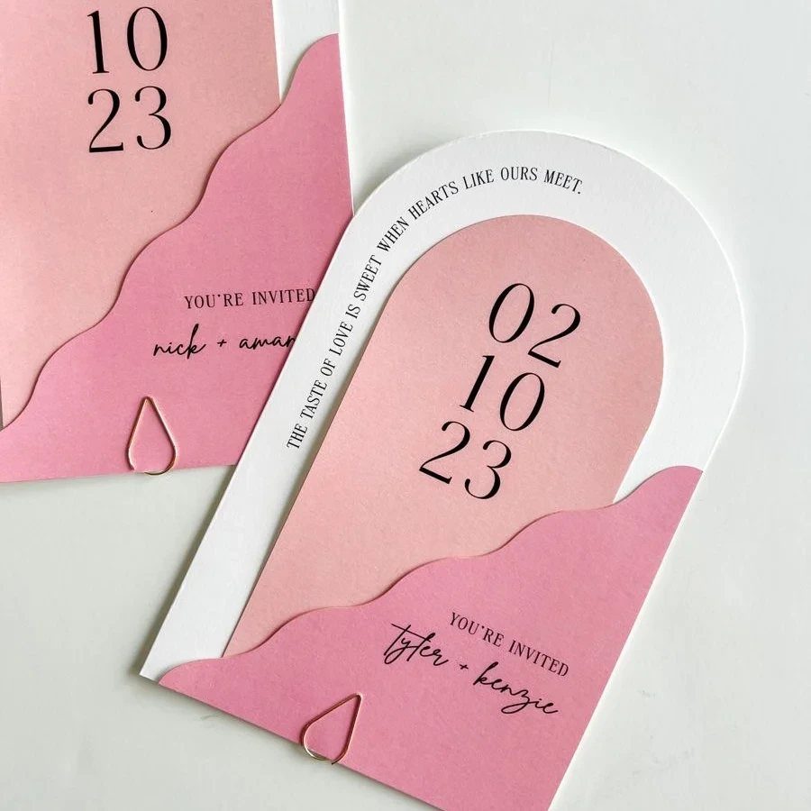 Arched pink and white wedding invitations with clean typography and layered paper edges.
