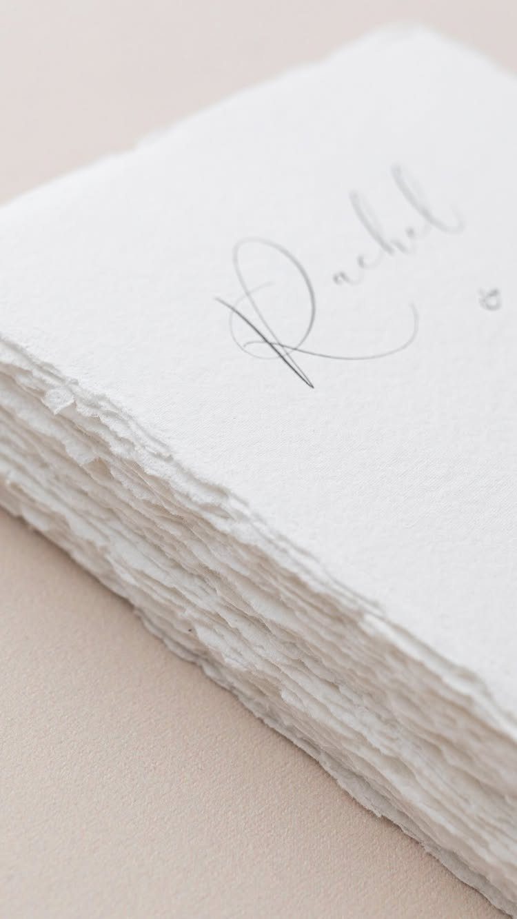 Stack of white handmade paper wedding invitations with elegant cursive calligraphy.