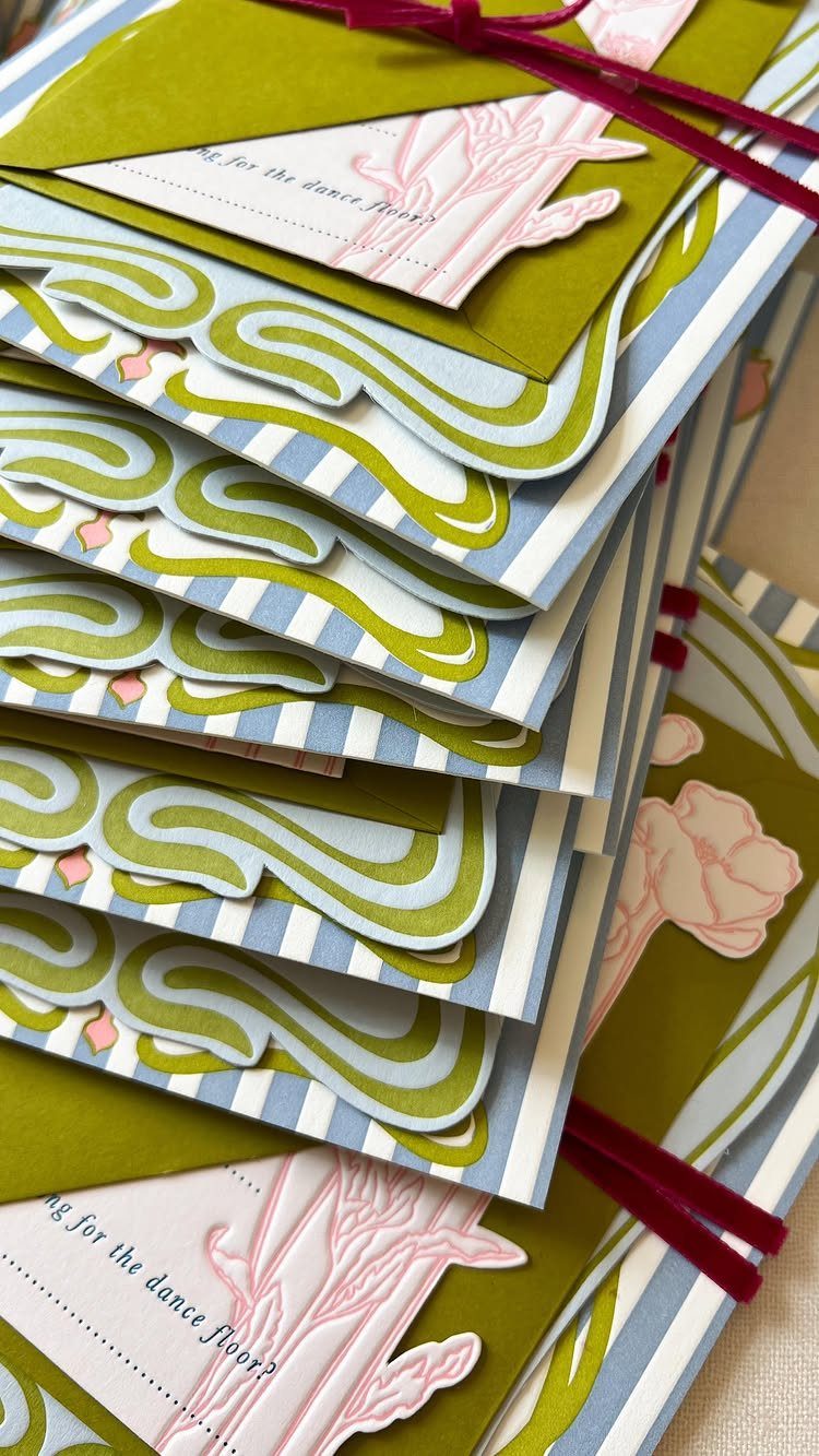 Layered wedding invitations with olive green and blue stripes and pink floral accents.