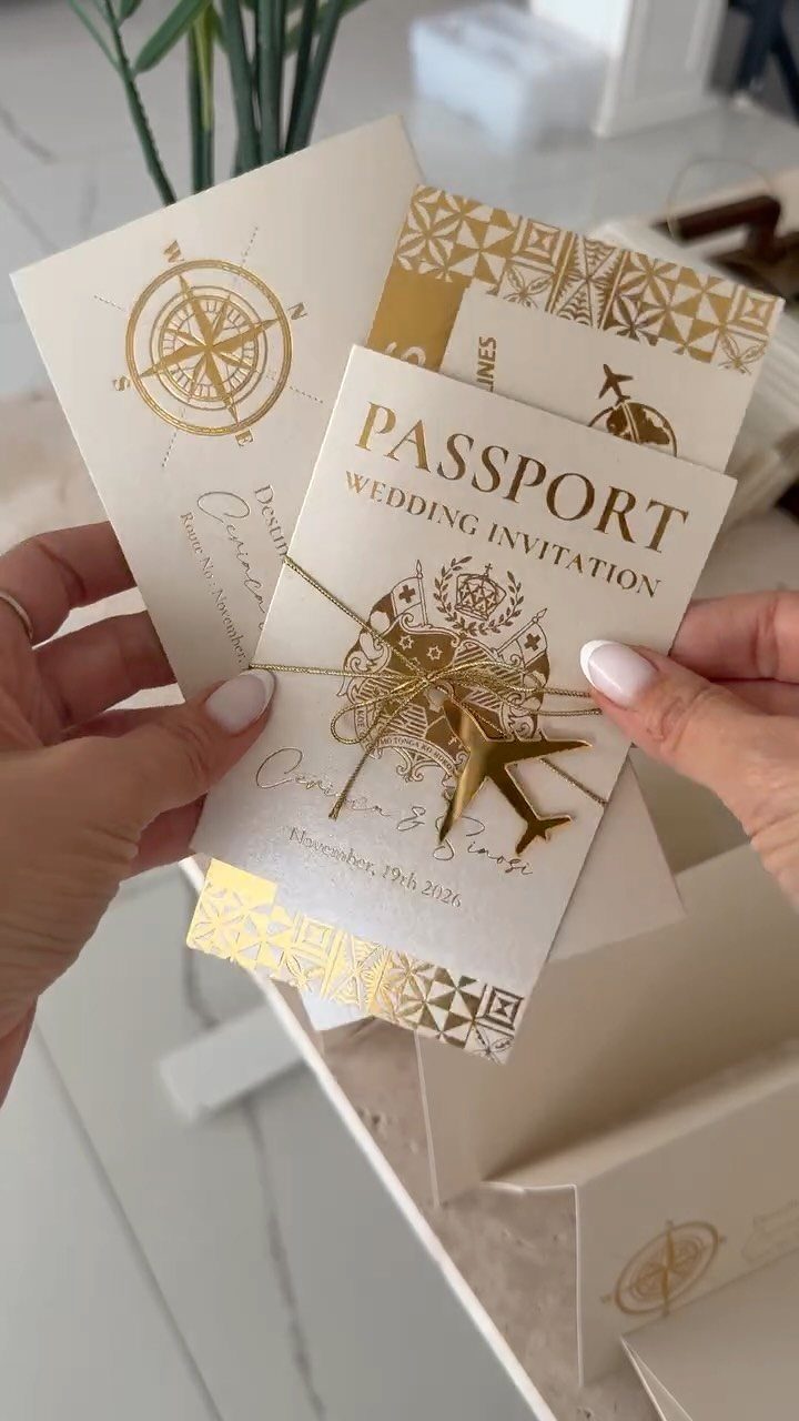 Passport style wedding invitations with gold foil compass and airplane designs.